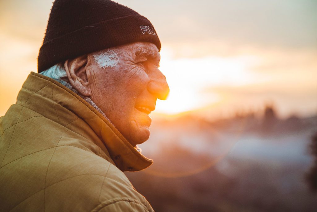 older man with hat against sunset