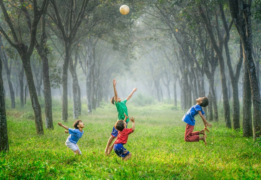 boys jumping after ball and playing by trees